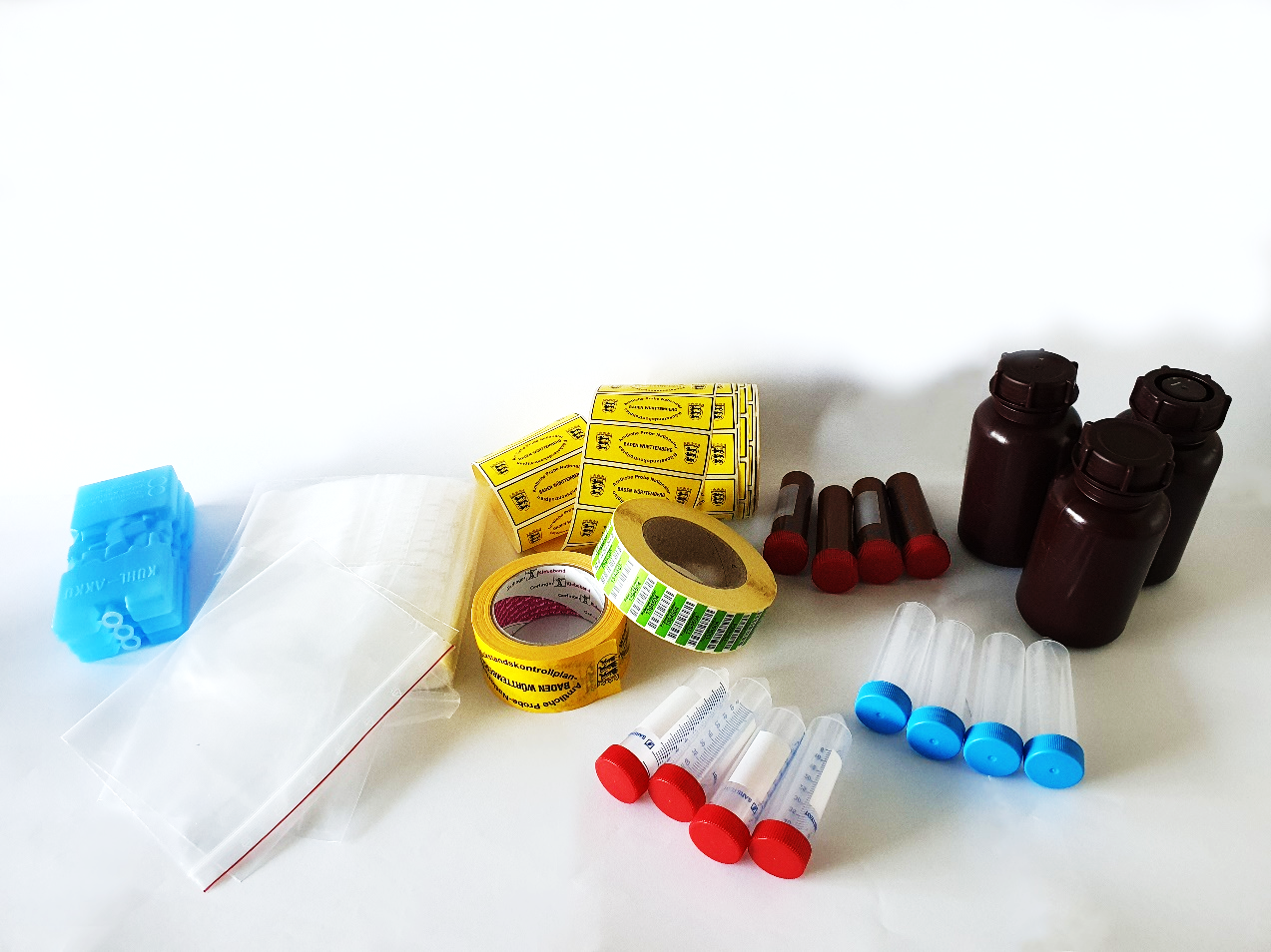 Auf dem Bild sind durchsichtige Probengefäße für Urin und Plasma, Plastikbeutel, braune Gefäße für Milchproben, Kühlakkus für den Probenversand, Etiketten und NRKP-Klebeband zu sehen.